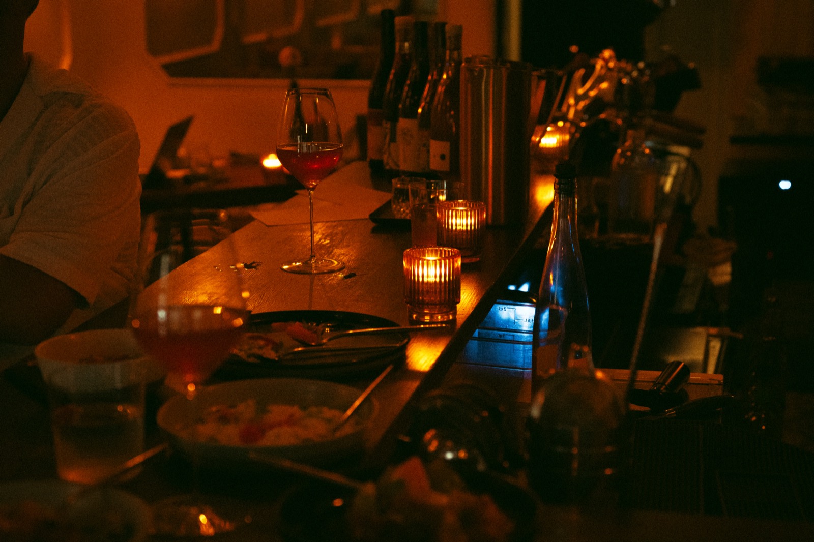 The bar at WEST10WEST by candlelight late in the evening, with wine glasses and share plates along the counter