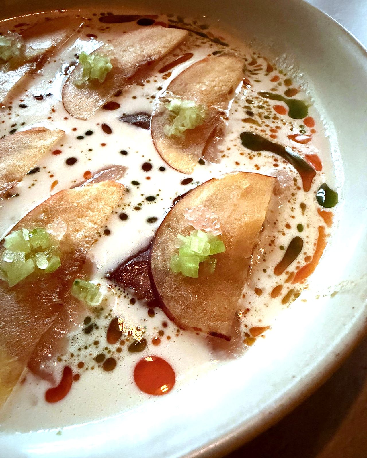 Close-up of hamachi under nectarine slices and bitter melon in a pool of ajo blanco with basil and chili oils at WEST10WEST, West Village NYC