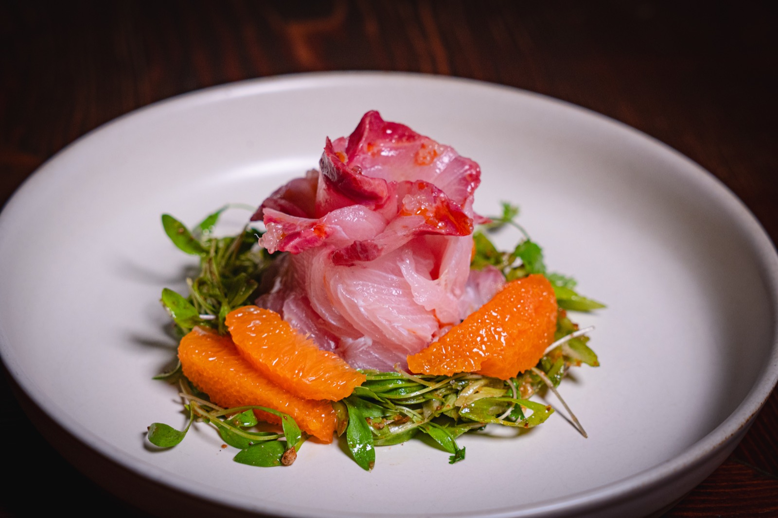 Hamachi crudo with blood orange, scallion, sesame and micro cilantro on a white plate at WEST10WEST, a West Village share-plates restaurant