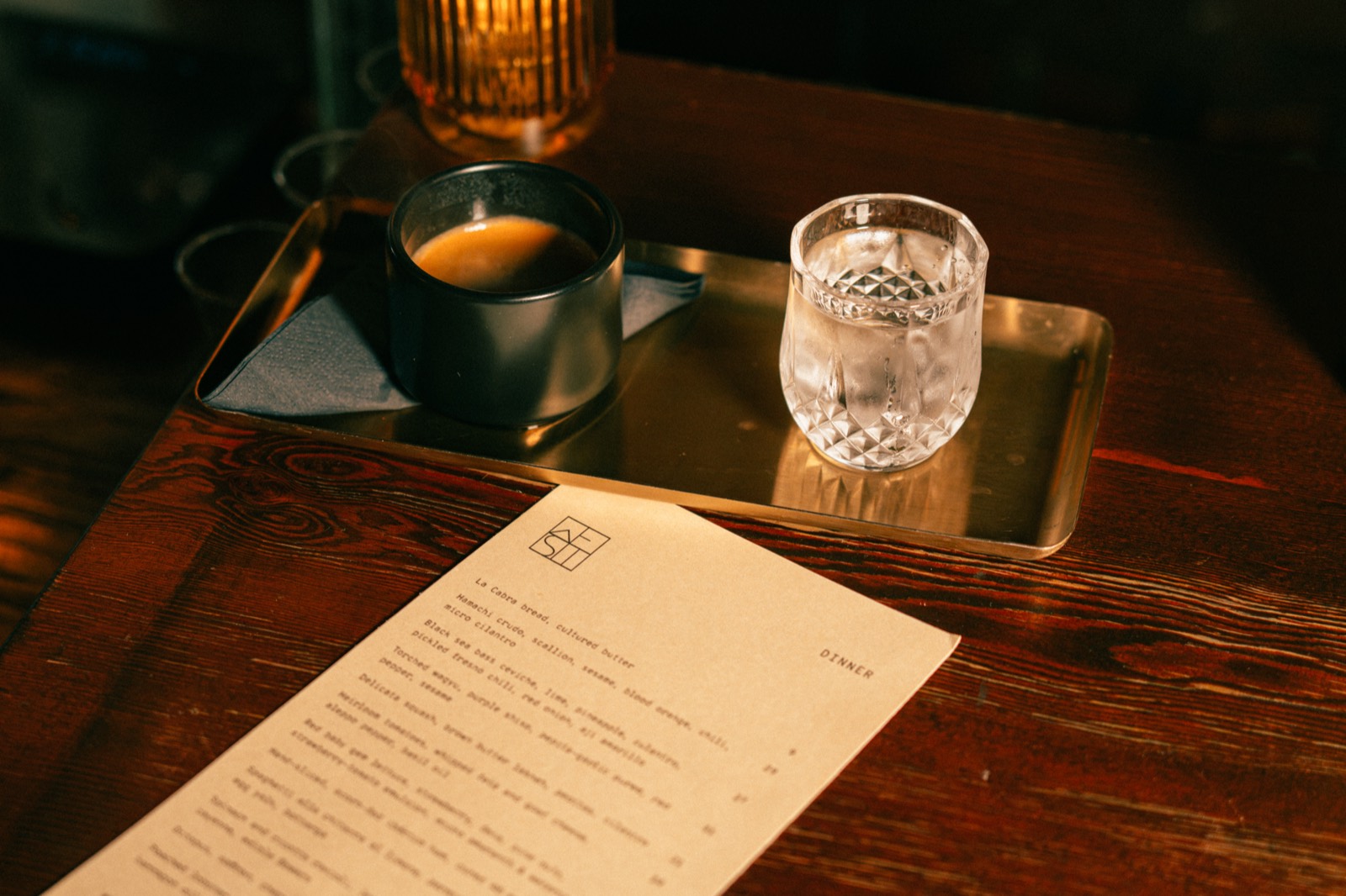 The single-page menu beside espresso and water on a brass tray at WEST10WEST on West 10th Street