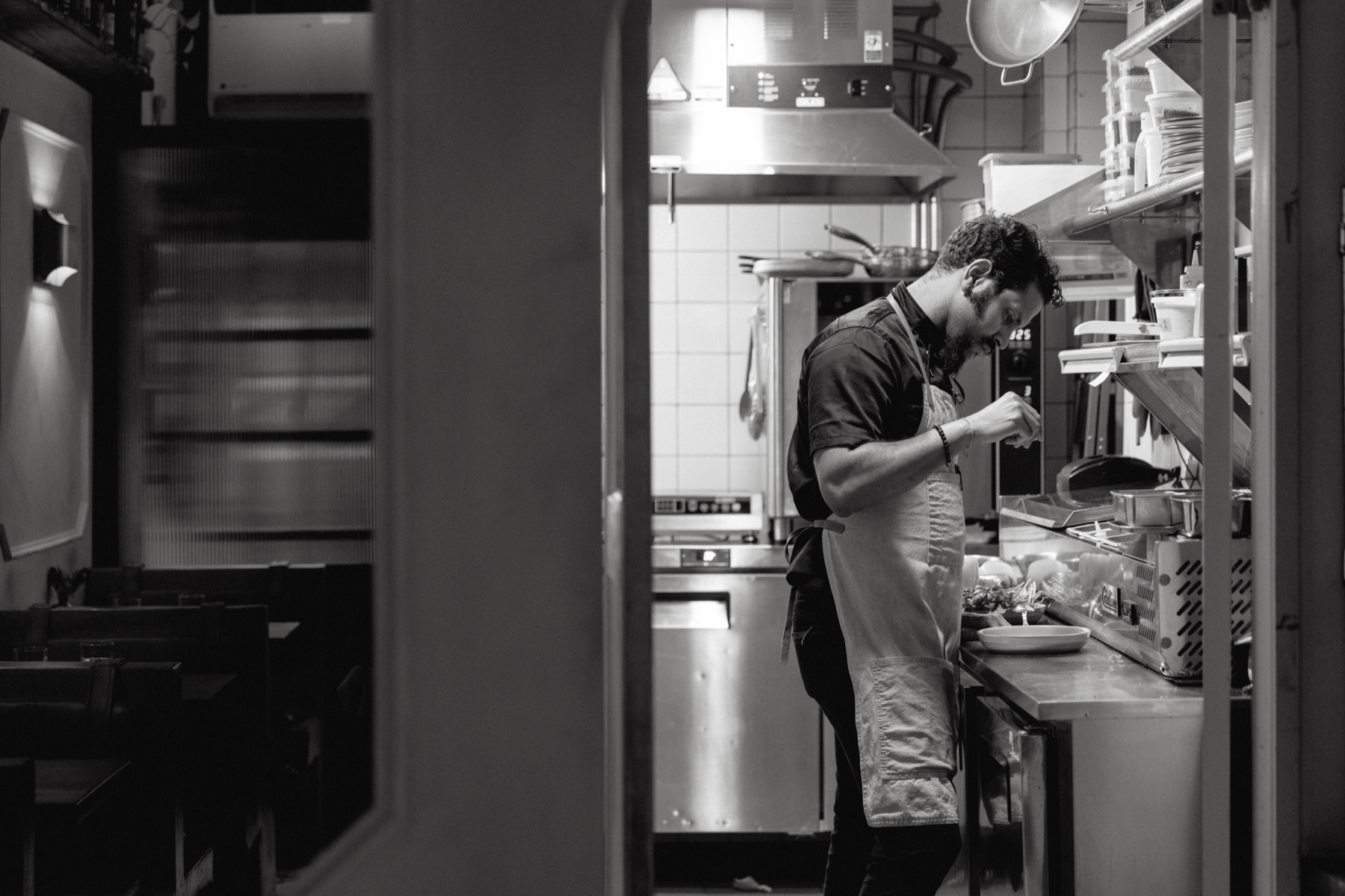 A cook at the stove mid-service, in black and white