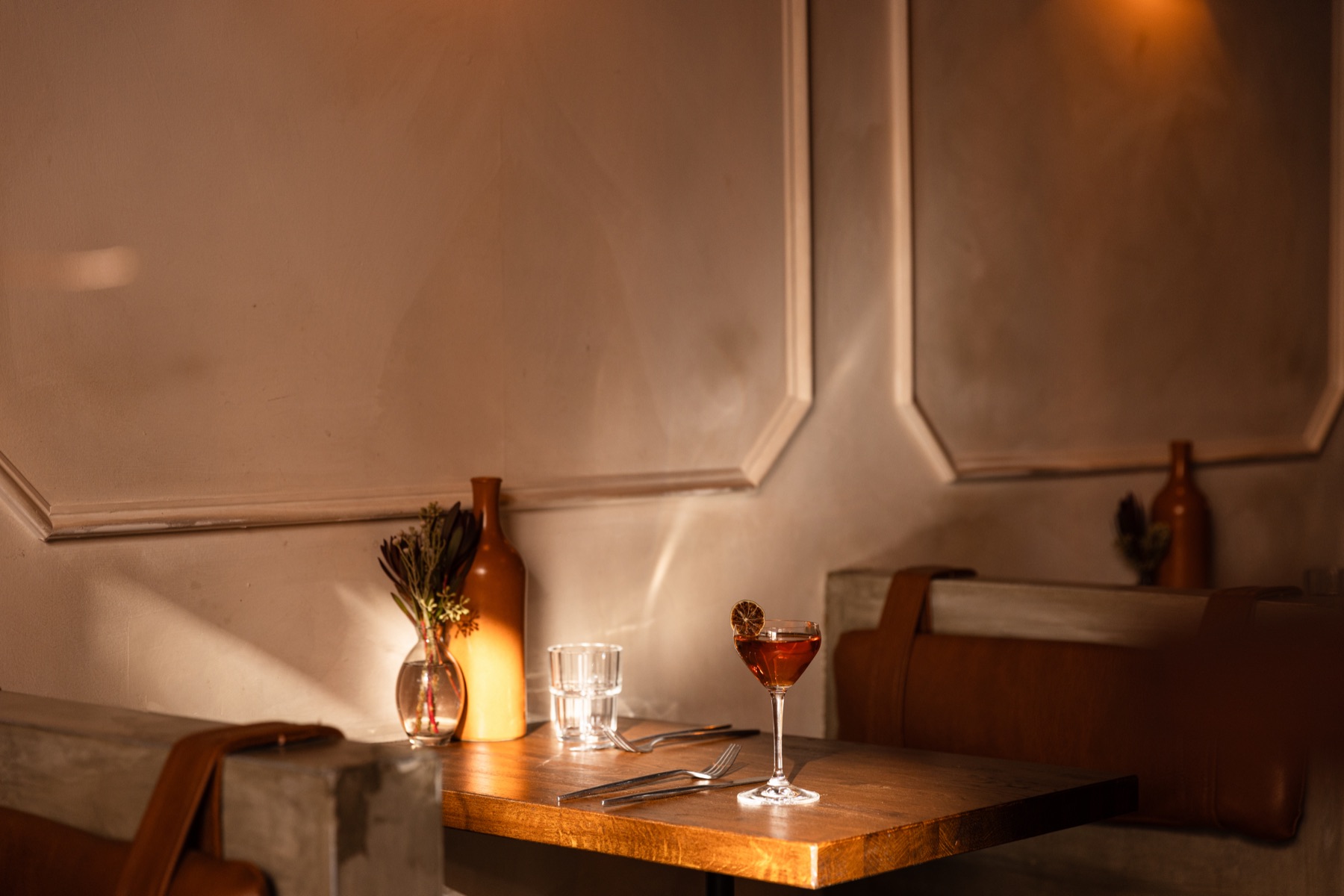A sunlit corner table with a cocktail and bud vase